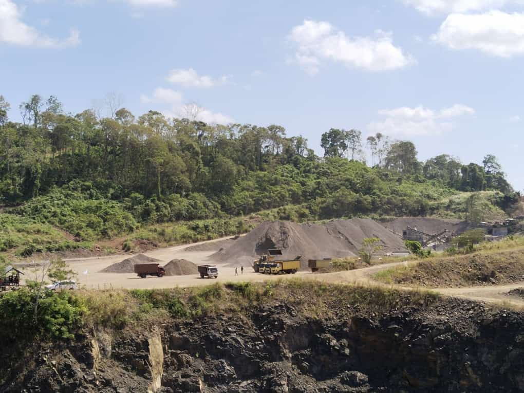 Tambang Petangis: jenjang kerja, jalan angkut, tumpukan agregat, dan unit pengolahan dengan latar hutan.